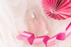 New Year's perfume. Blank women's perfume bottle mockup on beige fabric background with waves, pink satin ribbon, paper Christmas toy. photo