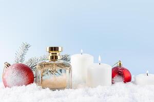 New Year's presentation of eau de toilette or perfume in a chic bottle with a golden cap. snow, red balls, spruce branches, candles. Front view photo
