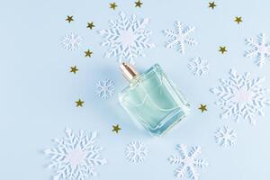 An unbranded perfume bottle on a blue background among decorative snowflakes and golden stars. top view. A copy space. blank bottle mockup. template photo