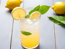 Close up high angle view of lemonade juice in glass on white wooden table adorned with lemon sliced and mint leaf decorated by two lemon fruit photo