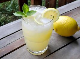 Close up high angle view of lemonade juice in glass on wooden table adorned with lemon sliced and mint leaf decorated by one lemon fruit photo