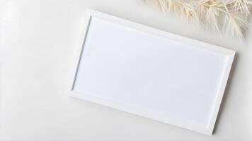 Top view blank space white rectangle frame mock up adorned by white paper plant on white table for creative design photo