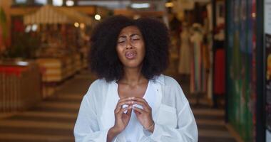 Anxious, worried and stressed African American woman, wearing white casual wear, expressing worries, stress and disappointment, crossing her hands while looking at camera over blurred store interior video
