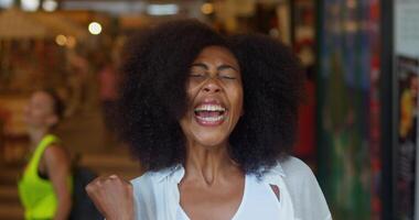 Cheerful happy delighted amazed African American pretty woman in casual clothes, rejoicing expressing astonishment, clenching fist from happiness, clapping hands, dancing in a blurred public place video