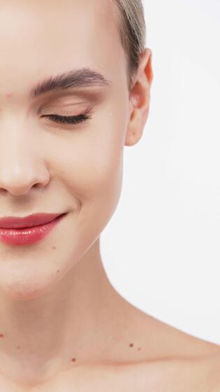 A young woman with radiant skin stands against a dark backdrop, showcasing her natural nude makeup. Her tender touch to her face emphasizes the importance of self-care and beauty 51427825 Stock Video at Vecteezy