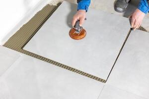 Tiler worker placing or tiling gray ceramic tile in the position over adhesive glue with lash tile leveling system, renovation or recontruction, concept of building photo