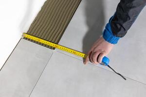 Tiler worker placing or tiling gray ceramic tile in the position over adhesive glue with lash tile leveling system, renovation or recontruction, concept of building photo
