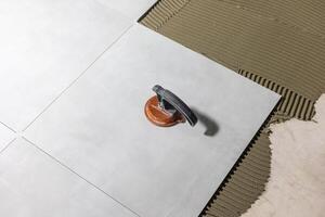 Tiler worker placing or tiling gray ceramic tile in the position over adhesive glue with lash tile leveling system, renovation or recontruction, concept of building photo
