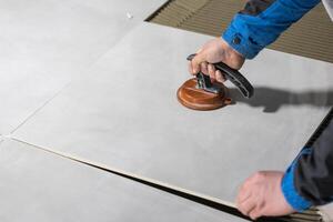 Tiler worker placing or tiling gray ceramic tile in the position over adhesive glue with lash tile leveling system, renovation or recontruction, concept of building photo
