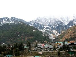 Dark cloudy Sky with snow-covered mountains and tall trees in Himachal Pradesh India photo