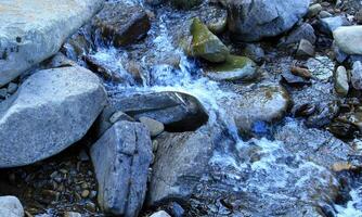 A stream of water flows in a stream, bending around boulders and stones photo