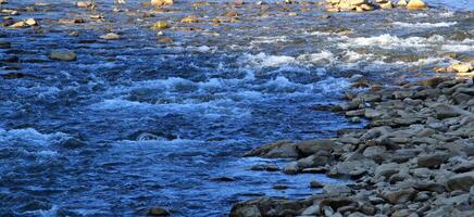 A stream of water flows in a stream, bending around boulders and stones photo