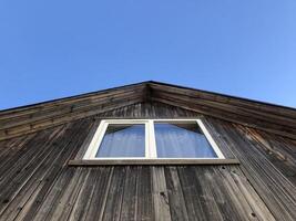 white window on the gable of a rustic wooden house, blue sky, low angle view photo