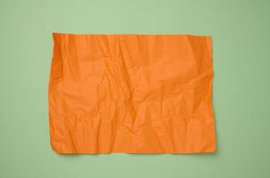 Crumpled rectangular sheet of orange paper on a green background, top view. Place for inscription photo