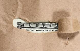 A hundred dollar bill peeks out through a hole in brown paper photo