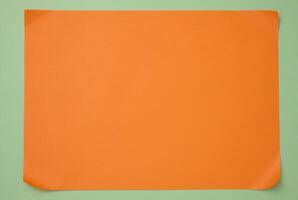 Blank orange sheet of paper on green background, abstract backdrop for inscription, copy space photo