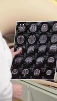 Woman doctor radiologist explains good results of CT scanning patient, showing the snapshot with images, observing and analyzing CT scan in modern clinic beside modern CT scanner video