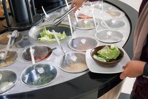 Fresh Salad bar counter with someone's hands lifting vegetables into a bowl. photo