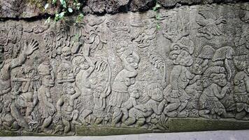 Intricately Carved Stone Wall Depicting Mythical Monkey Figures in a Lush Outdoor Setting Surrounded by Vines and Moss photo