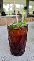 Refreshing iced black tea with mint garnish in a textured glass featuring a paper straw on a rustic outdoor cafe table setting for a relaxing beverage break photo