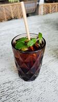Refreshing iced black tea with mint garnish in a textured glass featuring a paper straw on a rustic outdoor cafe table setting for a relaxing beverage break photo