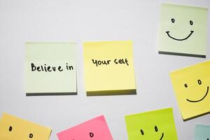 Believe in yourself and smile emoticon on sticky notes. Motivational words for personal development, inspirational handwriting. Isolated on background photo