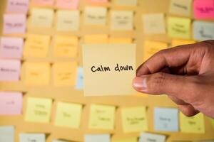 Hand hold sticky notes with words Calm Down. Motivational words for personal development, inspirational handwriting. Sticky notes background photo