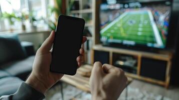 Enthusiastic Fan Watching American Football Game on TV While Checking Scores on Smartphone in Cozy Living Room photo