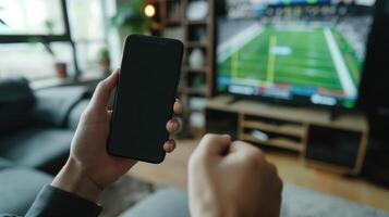 Watching American Football Game on TV While Holding Smartphone in Hand, Celebrating Touchdown, Modern Living Room Setting, Sports Enthusiast, Technology and Entertainment, Indoor Activity photo