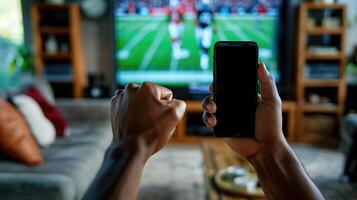 Enthusiastic Fans Watching American Football Game on TV and Celebrating with Mobile Phone in Hand, Living Room Setting, Sports Enthusiasm, Game Day Excitement, Modern Technology in Sports Viewing photo