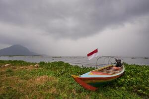 A wooden boat moored on the edge of a lake under cloudy sky photo