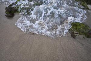 Close up of waves on sandy beach and coral reef covered by moss photo