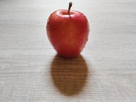Single red apple with water drops isolated on wooden background. Close up view of natural fruits photo concept.
