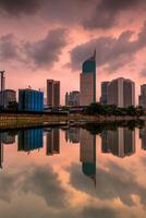 Jakarta skyline under cloudy sky. Office buildings tower of Jakarta city reflected on water with clouds on sky photo