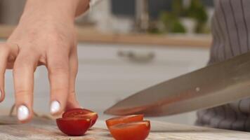 ein Koch vorsichtig Scheiben reif Tomaten im Hälfte mit ein Scharf Messer auf ein Küche Arbeitsplatte. video