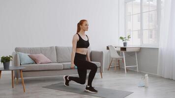 A woman is engaged in a fitness workout in her stylish living room, doing lunges while holding dumbbells. Bright sunlight filters through the window, creating an inviting atmosphere. video