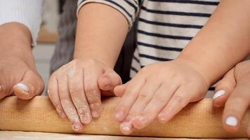 A parent and child work together, pressing their hands on a rolling pin to flatten dough while surrounded by flour in a warm kitchen. video