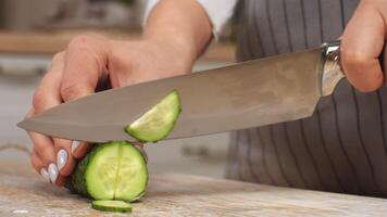 A hand holds a knife while cutting a cucumber on a wooden surface, showcasing the cooking process. video