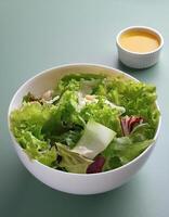 Fresh salad in a white bowl with dressing on the side isolated on a minimalist background photo