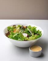 Fresh salad in a white bowl with dressing on the side isolated on a minimalist background photo