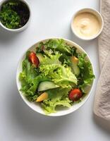 Fresh salad in a white bowl with dressing on the side isolated on a minimalist background photo