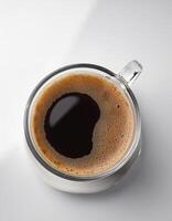 A cup of black coffee with froth on top, placed on a white surface photo