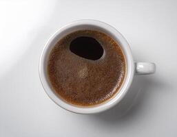 A cup of black coffee with froth on top, placed on a white surface photo