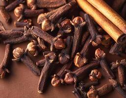 Cloves and cinnamon are spread on a brown background photo