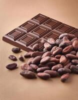 Dark chocolate bar with cocoa beans on light brown background photo