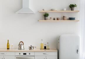 Modern minimalist white kitchen in scandinavian style, simple, minimalist interior. Refrigerator, shelves with crockery and plants in pots, furniture and stove with utensils, light wall, free space photo