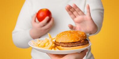 Unrecognizable plus size girl refusing to eat fast junk food, showing stop gesture with hand and choosing apple photo