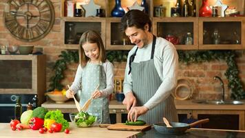 Loving dad teaching his little daughter to cook healthy food, preparing vegetable salad in kitchen together, cooking lunch or dinner, enjoying homemade meals, having fun at home, copy space photo