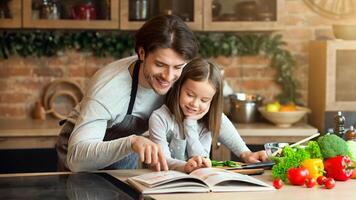 Happy dad and little daughter checking recipe in cookbook at kitchen together while cooking healthy lunch at home, free space photo