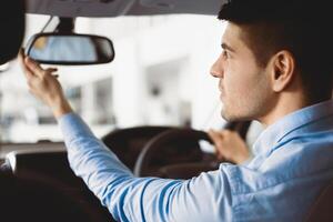 Young Man Touching And Looking At Rearview Mirror Sitting In Driver's Seat Testing New Auto photo